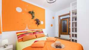 Une chambre avec un mur d’accent orange, un lit avec une literie à rayures, un grand miroir et une armoire.