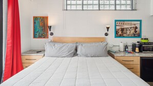 Ein Schlafzimmer mit Bett, Nachttisch, Kommode, einem Fenster mit Jalousien und einem Bild an der Wand.