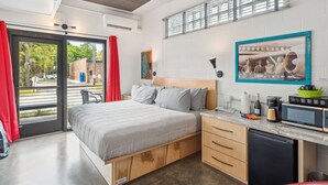 Ein kleines Hotelzimmer mit Bett, einer kompakten Küchenzeile, einem Essbereich und einer Glastür zum Außenbereich.