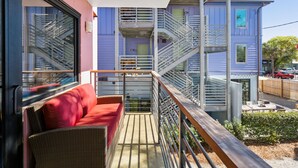 A balcony with wicker furniture, a metal railing, and a view of a multi-story building with a fire escape.