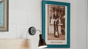 A bedroom with a bed, a framed photograph on the wall, and a wall-mounted lamp.