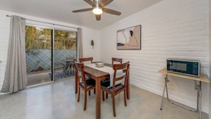 A dining area with a table and chairs, a ceiling fan, a microwave on a stand, and a sliding glass door leading to an outdoor area. - Cozy / Spotless / Central / Remodeled / 2 BR 1 BA (Tucson)