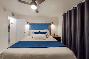Quarto de hotel com cama, ventilador de teto, mesa de cabeceira e janela com cortinas.