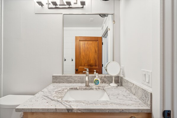 Un baño con lavamanos de mármol, puerta de madera y espejo.