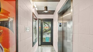 A hallway with a ceiling fan, a door with a glass panel, and an elevator.