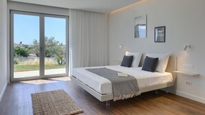 Une chambre à coucher moderne avec un grand lit, une vue dégagée grâce à une porte-fenêtre coulissante et un petit tapis sur le sol.