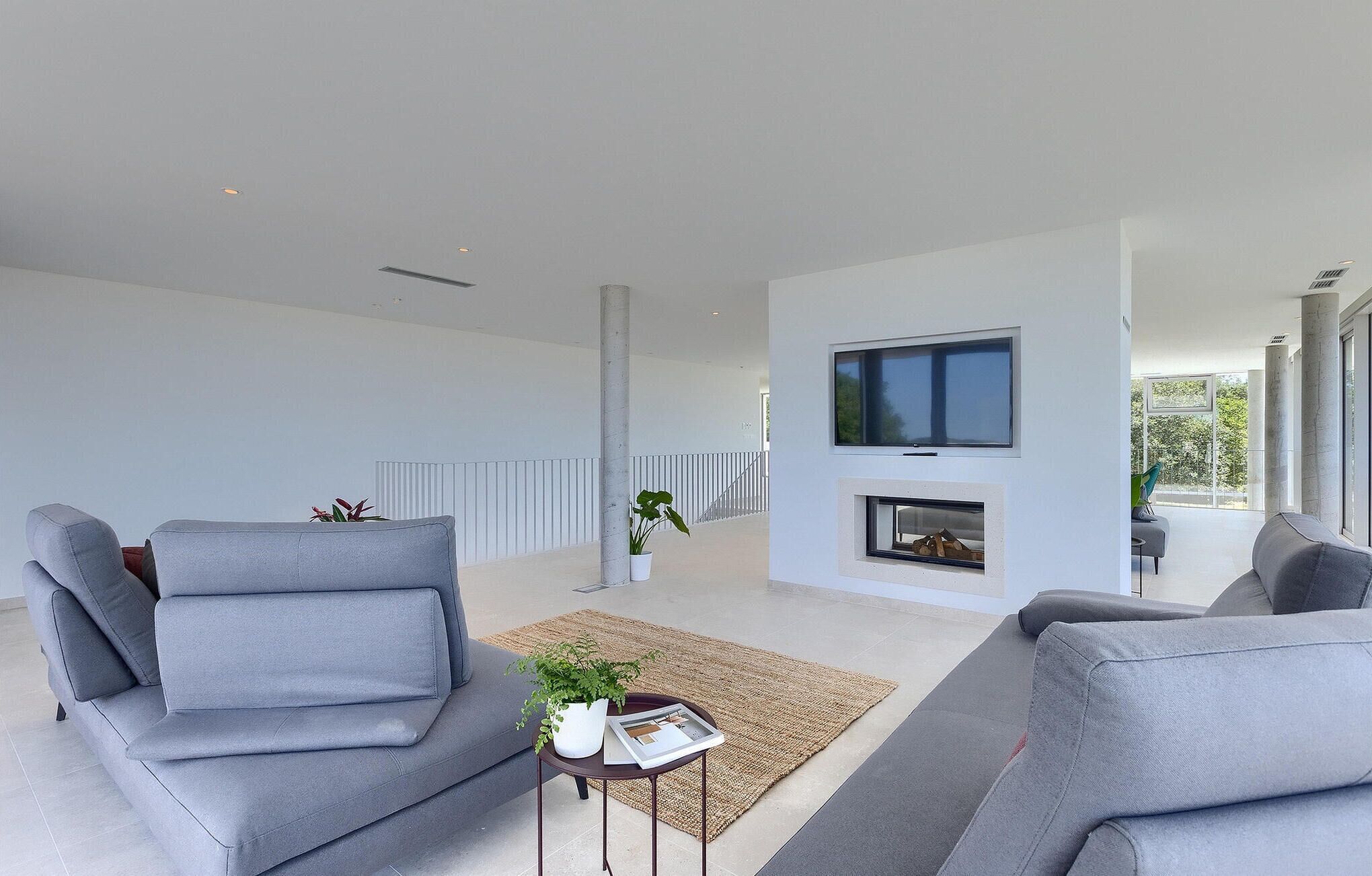 A modern living room with grey sofas, a flat-screen TV, a fireplace, and a view of the outdoors.