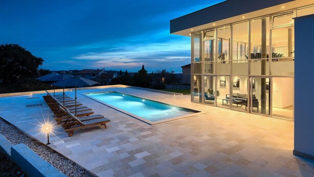 Une maison moderne dotée d’une piscine, de chaises longues et d’un patio vitré.