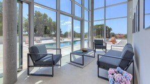 Un espace intérieur moderne doté de grandes fenêtres, d’une piscine et d’un espace extérieur aménagé pour s’asseoir.