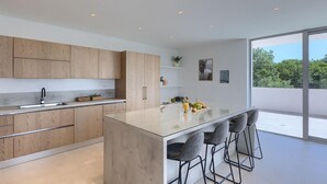 Une cuisine moderne avec des meubles en bois, un îlot central doté de tabourets de bar, une grande fenêtre et une vue sur la verdure environnante.