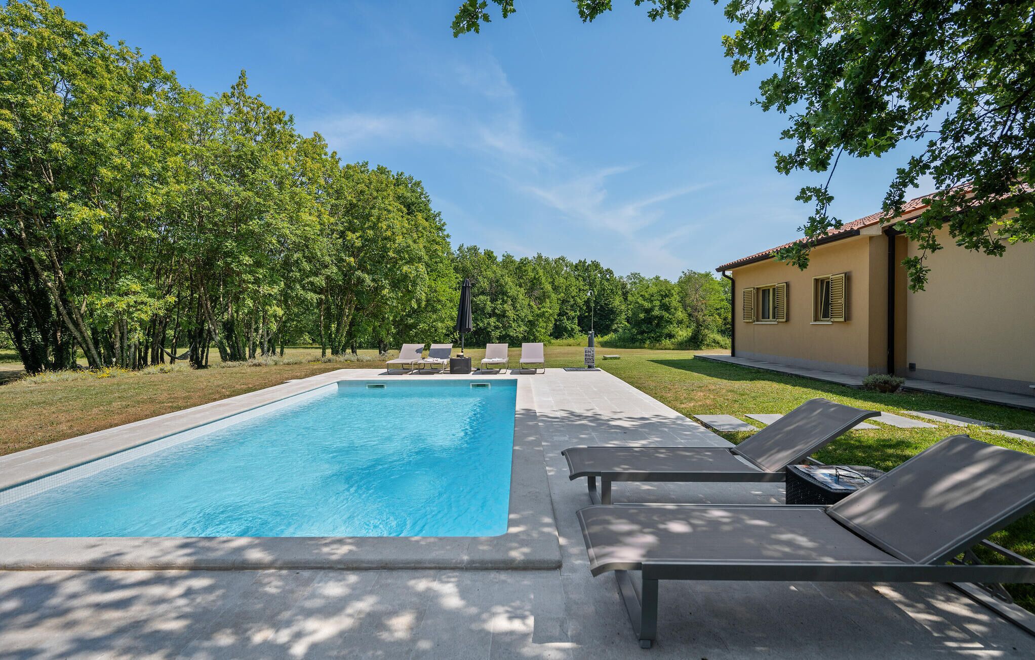A rectangular swimming pool with lounge chairs and a small building with shutters.