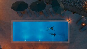 Une piscine hors sol où nagent deux personnes, entourée de chaises longues et de parasols.