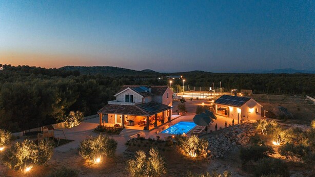 Une maison moderne dotée d’une piscine, de panneaux solaires et d’un espace extérieur bien éclairé au crépuscule.