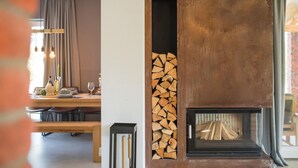Un salon moderne avec une cheminée, un coin repas avec une table et des chaises, et un espace cuisine équipé d’une cuisinière.