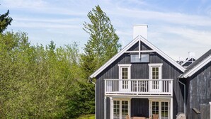 Une maison en bois à deux étages, dotée d’un balcon, d’une terrasse et d’un espace barbecue.