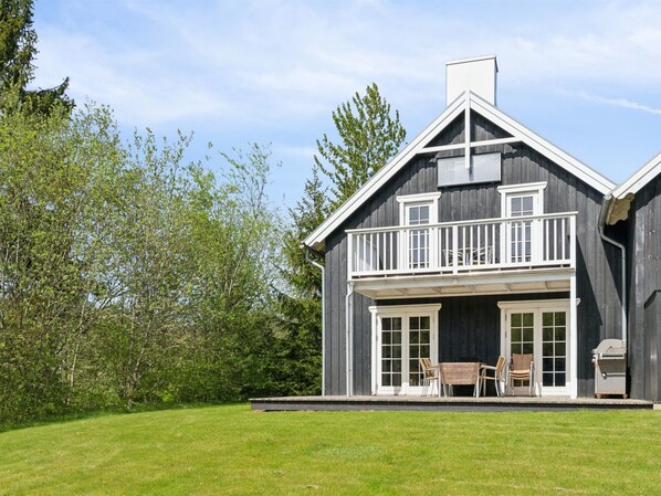 A two-story house with a balcony, large windows, and a grill outside.