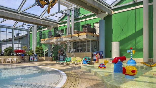 Une piscine intérieure dotée d’un toit en verre, de murs verts et de diverses structures de jeux.