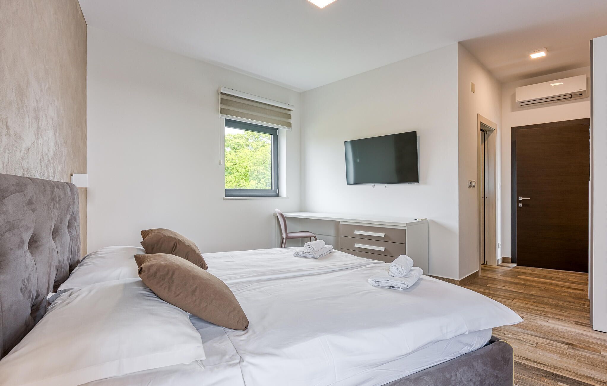 A modern bedroom with a large bed, a desk, and a TV.