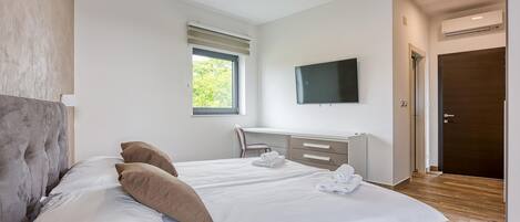 A modern bedroom with a large bed, a desk, and a TV.