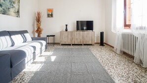 A living room with a sofa, a TV on a wooden cabinet, a radiator, and a window with sheer curtains. - Stunning home in Ponte Buggianese (Ponte Buggianese)