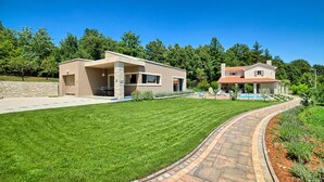 Une maison moderne à deux étages, dotée d’une pelouse bien entretenue et d’un chemin en briques incurvé menant à l’entrée.