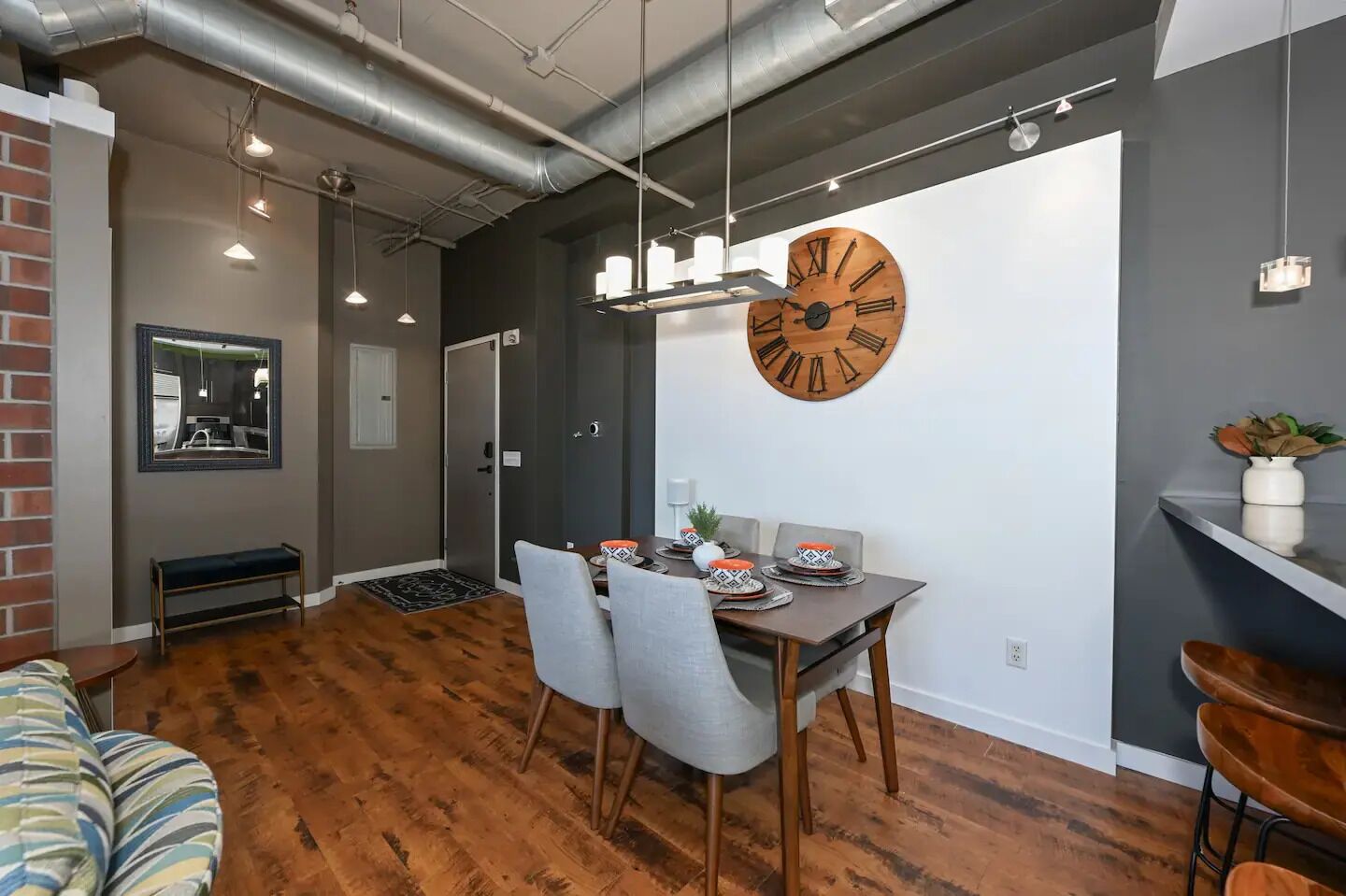 A modern dining area with a wooden table, grey chairs, and a large wall clock.