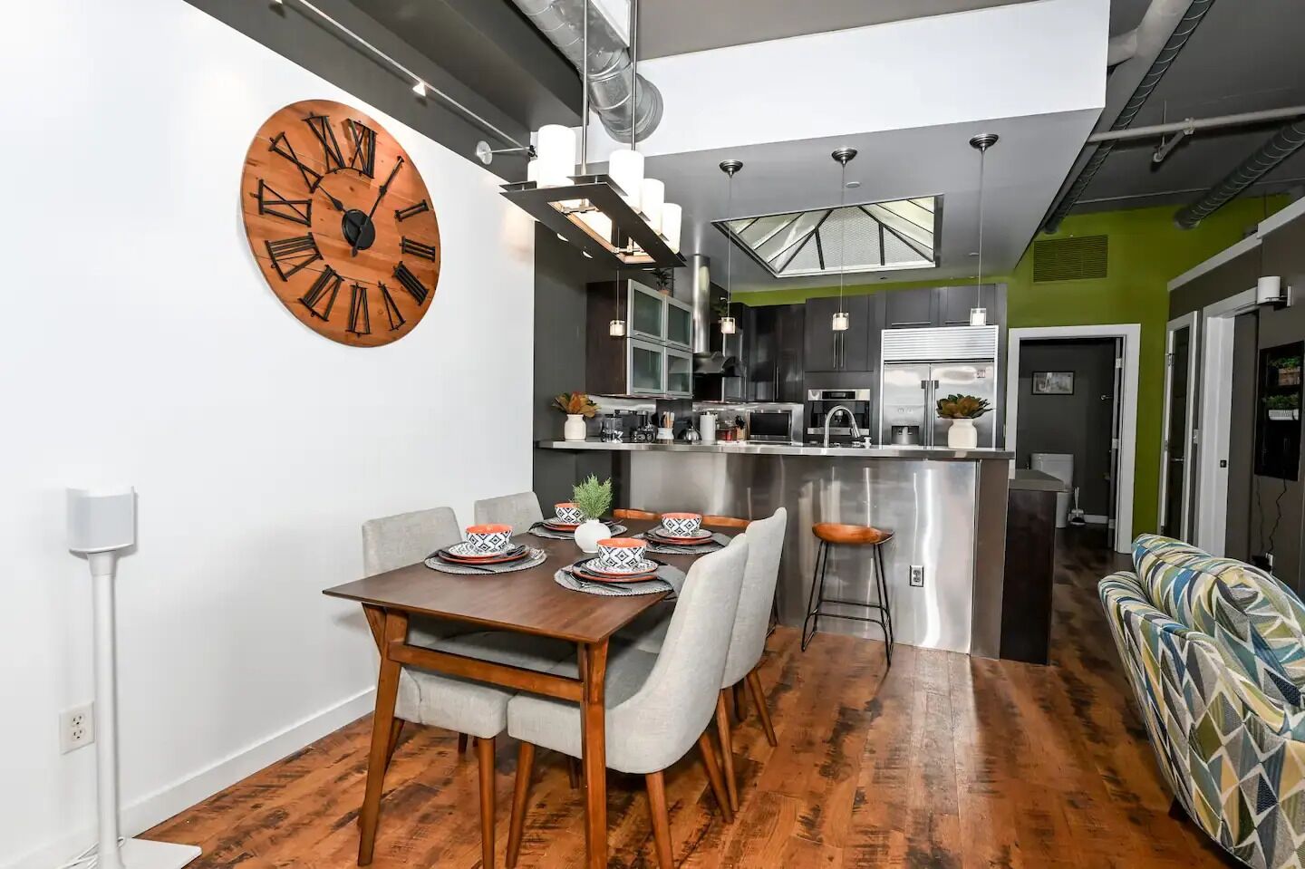 Une cuisine moderne dotée d’un îlot central, un coin repas avec une table et des chaises en bois, et un canapé à motifs dans l’espace de vie.