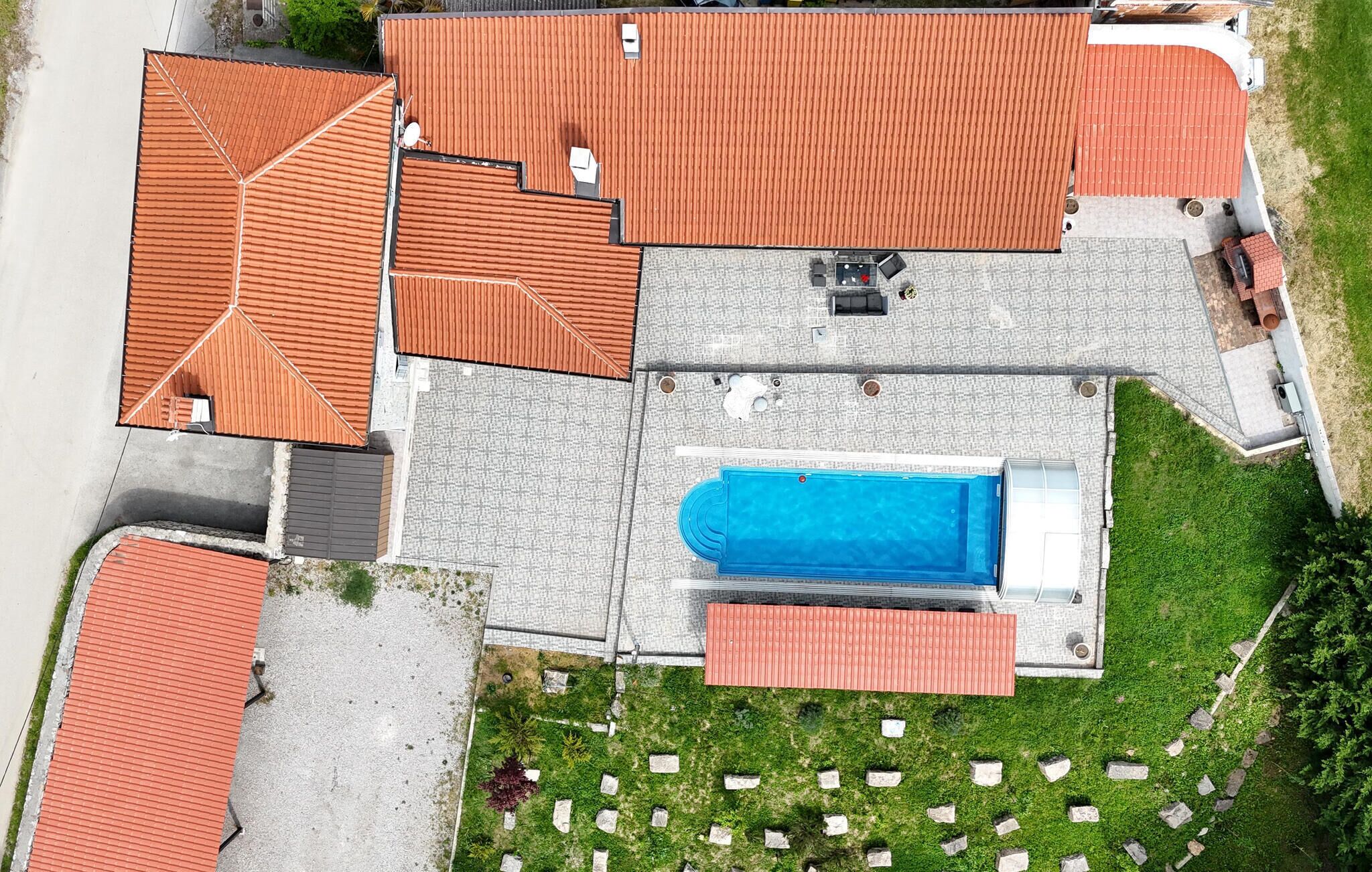 Vista aérea de una propiedad residencial con piscina, varios edificios con techos rojos y un césped bien cuidado con bordes de piedra.