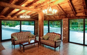 A room with two sofas facing each other, a wooden coffee table, and large windows offering a view of a garden and a greenhouse. - Lovely home in Motovun (Motovun)