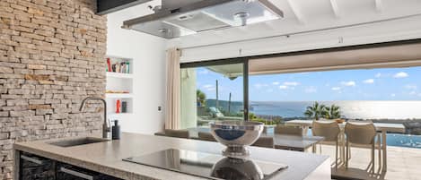 A modern kitchen with a large island, a stone wall, and a view of the ocean.