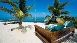 Vista de la playa con una cama de madera, palmeras y un cielo azul despejado.