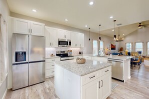 A modern kitchen with white cabinetry, stainless steel appliances, and a granite countertop island.