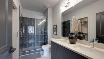 Un baño moderno con cabina de ducha de vidrio, inodoro blanco, espejo grande y tocador con lavamanos.