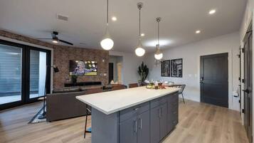 A modern kitchen with a central island, pendant lighting, and a brick accent wall.