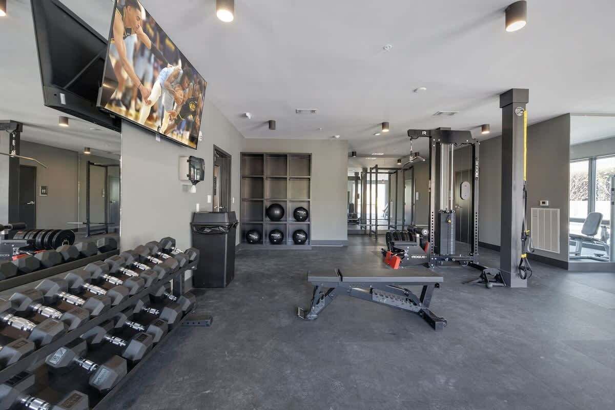 A modern gym with weightlifting equipment, a television, and a mirrored wall.