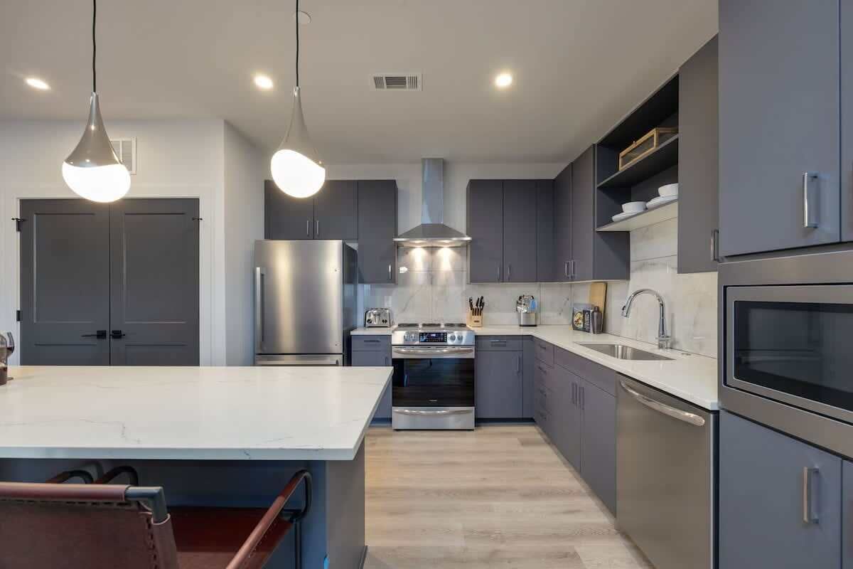 A modern kitchen with grey cabinets, stainless steel appliances, and pendant lighting.