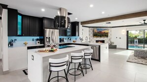 A modern kitchen with a central island, bar stools, and a large window overlooking a pool.