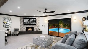 A modern living room with a fireplace, a pool view, and a ceiling fan.