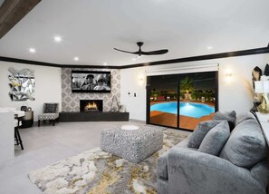 A modern living room with a fireplace, a pool view, and a ceiling fan. - Modern Roose-Pool-Spa-Fire Pit-Mins to Old Town! (Scottsdale)