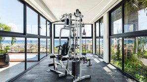 Une salle de sport avec vue sur l’océan, de grandes fenêtres et du matériel d’exercice.