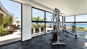Ein modernes Fitnessstudio mit großen Fenstern, die einen Pool und Meerblick bieten.