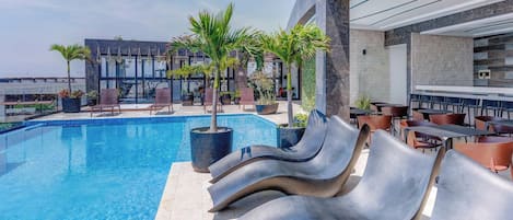 A pool area with lounge chairs, a dining area, and a building with a modern design.
