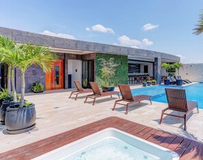 A modern outdoor pool area with lounge chairs, a hot tub, and a restaurant with outdoor seating. - Oceanview Infinity Pool, Steps to 5th Ave & Beach (Playa del Carmen)