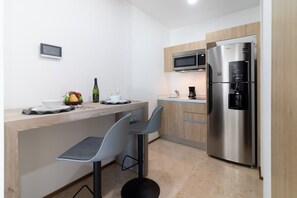 Une cuisine moderne équipée d’un réfrigérateur en acier inoxydable, d’un four à micro-ondes et d’un plan de travail en bois. On y trouve deux tabourets de bar et un petit îlot central sur lequel sont posés un saladier rempli de fruits et une bouteille.