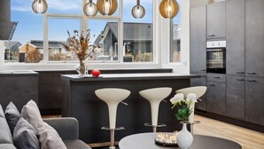 Een moderne keuken met grote ramen, hanglampen en uitzicht op de omgeving.