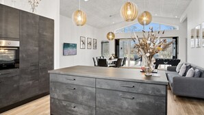 Een moderne keuken met een groot keukenblok, donkere kasten en hanglampen.