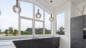 Een moderne keuken met donkere kastjes, een groot raam en hanglampen.