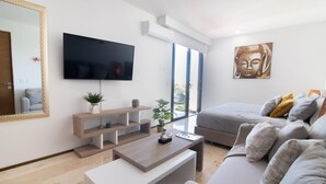 A modern living room with a flat-screen TV, a sofa, a coffee table, and a large window with a view. - Chic Retreat with Oceanview Roof Pool Near 5th Ave (Playa del Carmen)