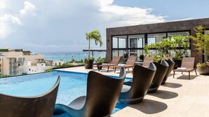 A rooftop pool area with modern lounge chairs, a clear view of the ocean, and a building with large windows. - Chic Retreat with Oceanview Roof Pool Near 5th Ave (Playa del Carmen)