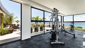 A modern gym with large windows overlooking a pool and ocean view. - Chic Retreat with Oceanview Roof Pool Near 5th Ave (Playa del Carmen)
